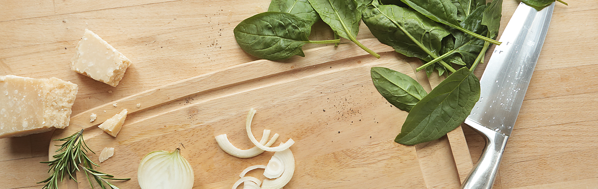Spinat, Zwiebeln, Käse, Gewürze und Messer auf einen Holzbrett